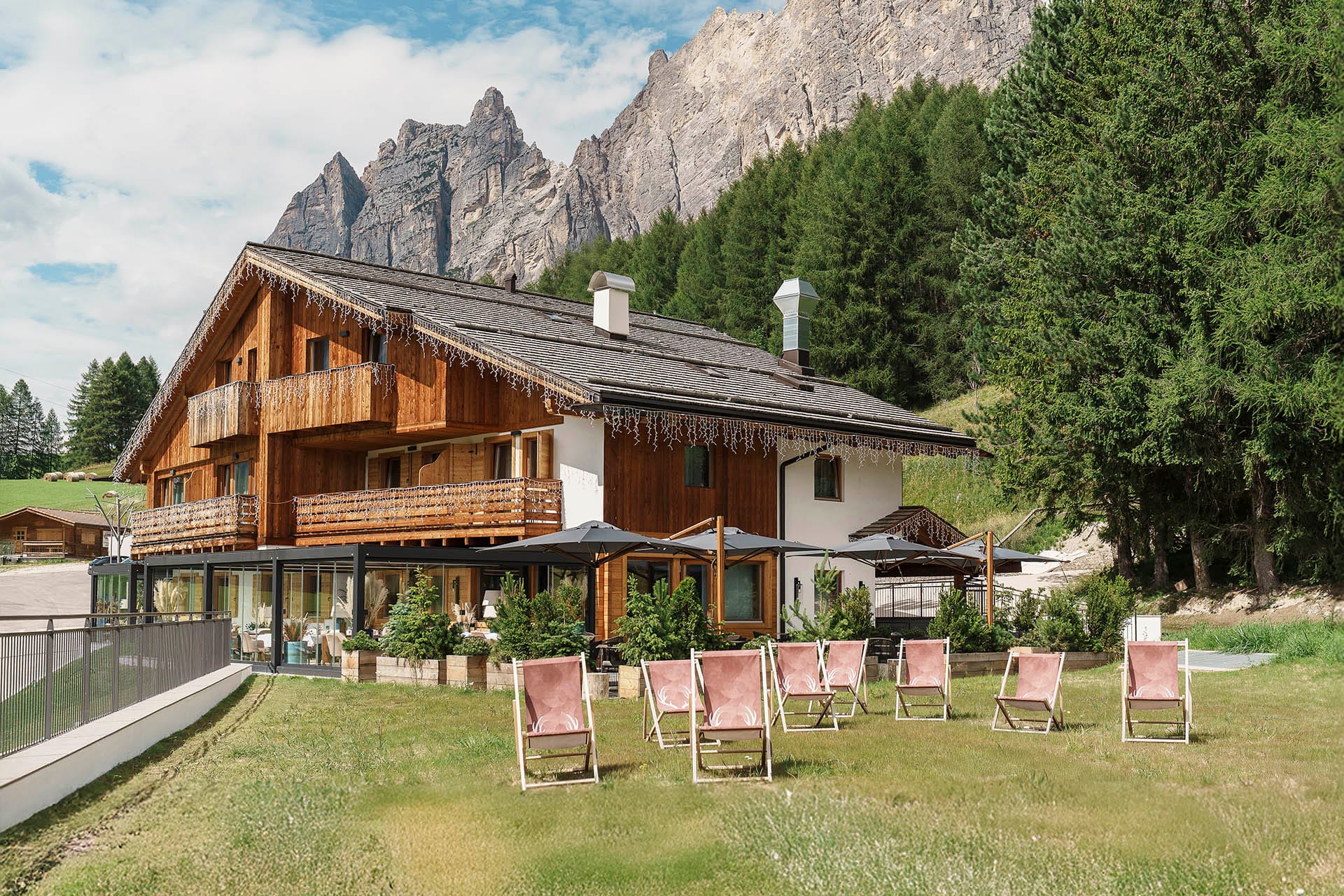 Facciata esterna Casa Guargnè Cortina d’Ampezzo durante l'estate con prato verde e sdraio